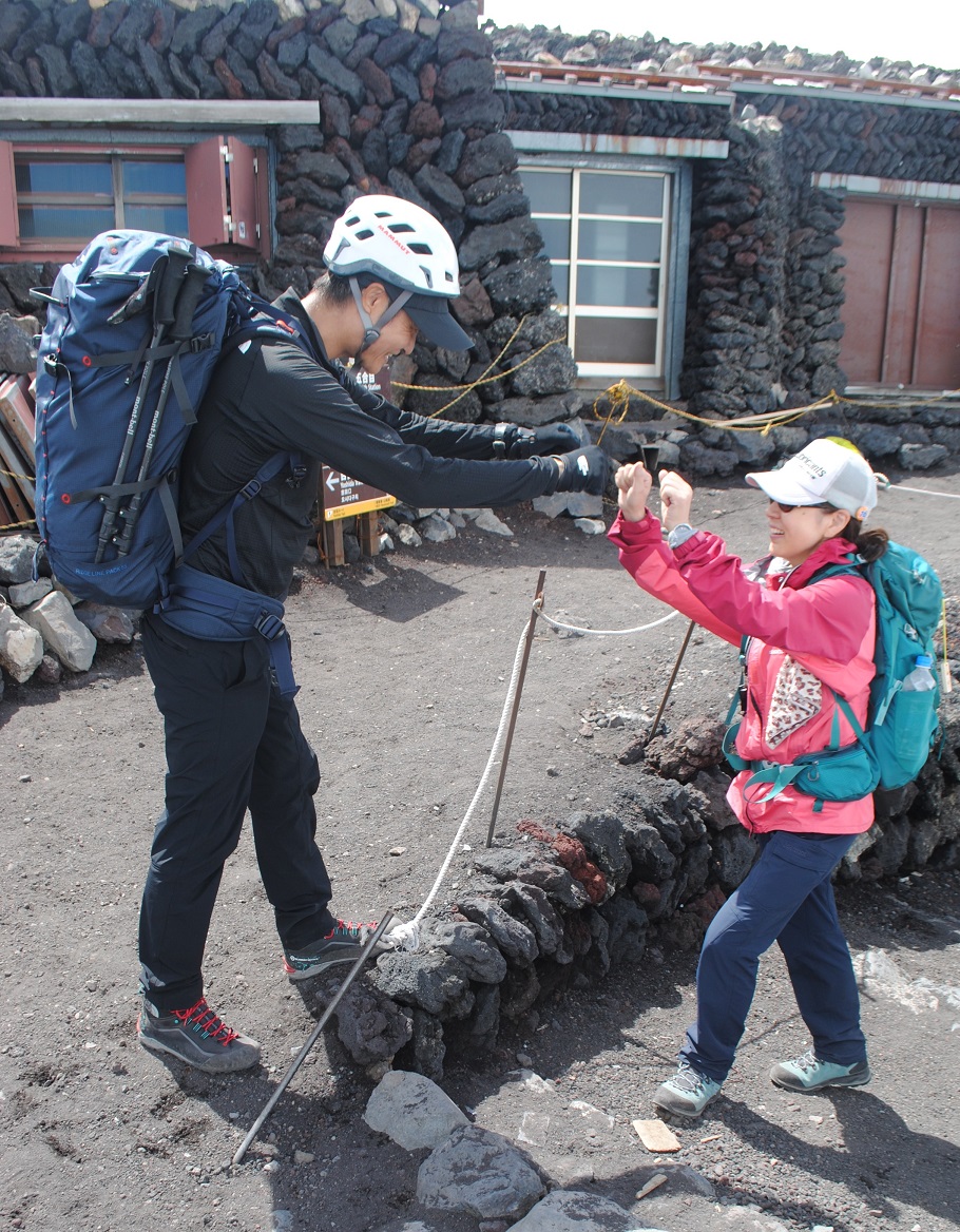 吉田口の山頂でグータッチをする高山ガイドと参加者